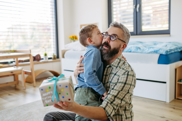 Dad get handmade gift from little son, present wrapped in diy homemade wrapping paper. Father embracing boy. Happy Fathers day concept.