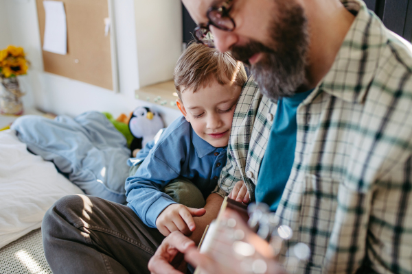 Father teaching boy to play on acoustic guitar. Mesmerized son listening dad making music. Concept of Fathers Day, and fatherly love.