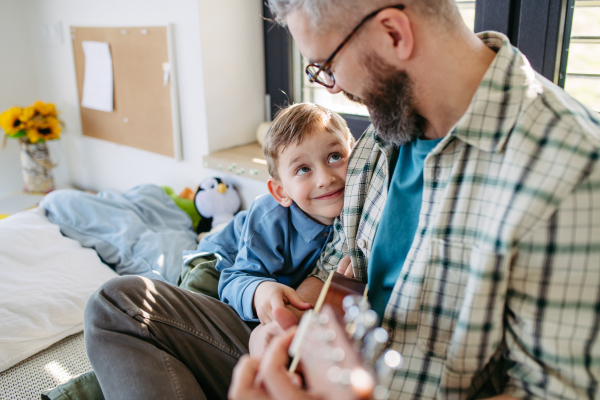 Father teaching boy to play on acoustic guitar. Mesmerized son listening dad making music. Concept of Fathers Day, and fatherly love.