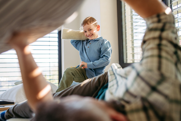 Pillow fight between young son and father. Dad spending time with son at home, having fun. Happy Fathers day concept.