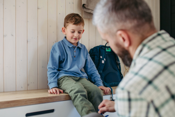 Father helping son get ready for kindergarten, preschool. Putting coat and shoes on, handing lunchbox with snacks.