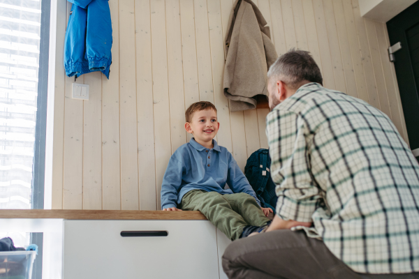 Father helping son get ready for a kindergarten, preschool. Putting shoes on.