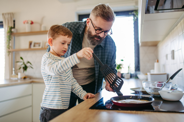 Boy helping father to make pancake. Father spending time with son at home, making snack together, cooking. Weekend activities for single dad with young boy. Fathers day concept.