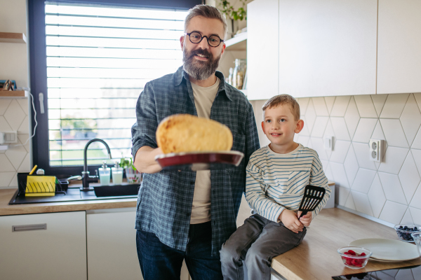 Boy helping father to make pancake. Son looking how father fliping pancake. Weekend activities for single dad with young boy. Fathers day concept.