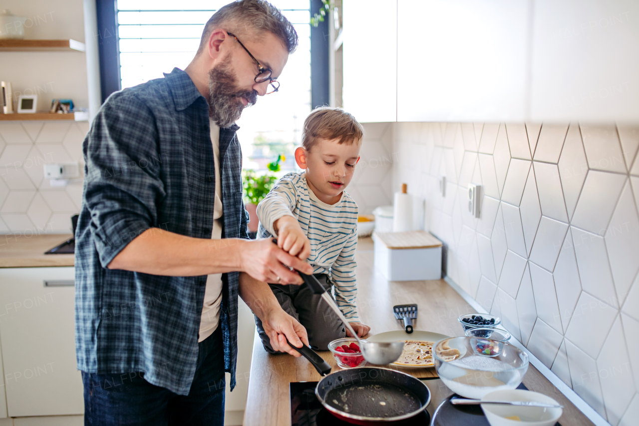 Boy helping father to make pancake. Father spending time with son at home, making snack together, cooking. Weekend activities for single dad with young boy. Fathers day concept.