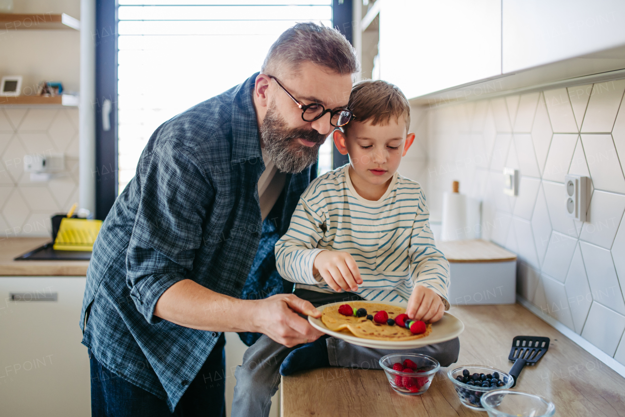 Boy filling pancake with fruit, sweets. Father spending time with son at home, making snack together, cooking. Weekend activities for single dad with young boy. Fathers day concept.