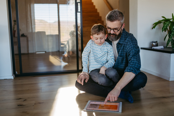 Father showing son smart home system, adjusting household functions, lighting, security cameras, door locks and thermostat or heating settings.