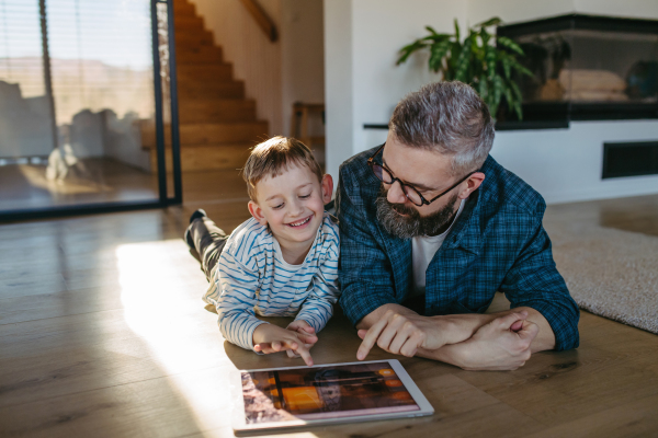 Father showing son smart home system, adjusting household functions, lighting, security cameras, door locks and thermostat or heating settings.