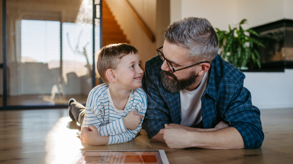 Father showing son smart home system, adjusting household functions, lighting, security cameras, door locks and thermostat or heating settings.