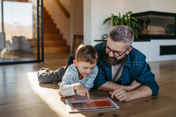 Father showing son smart home system, adjusting household functions, lighting, security cameras, door locks and thermostat or heating settings.