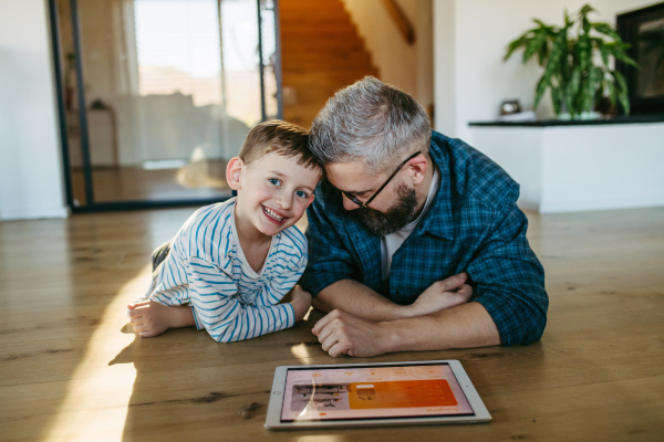 Father showing son smart home system, adjusting household functions, lighting, security cameras, door locks and thermostat or heating settings.