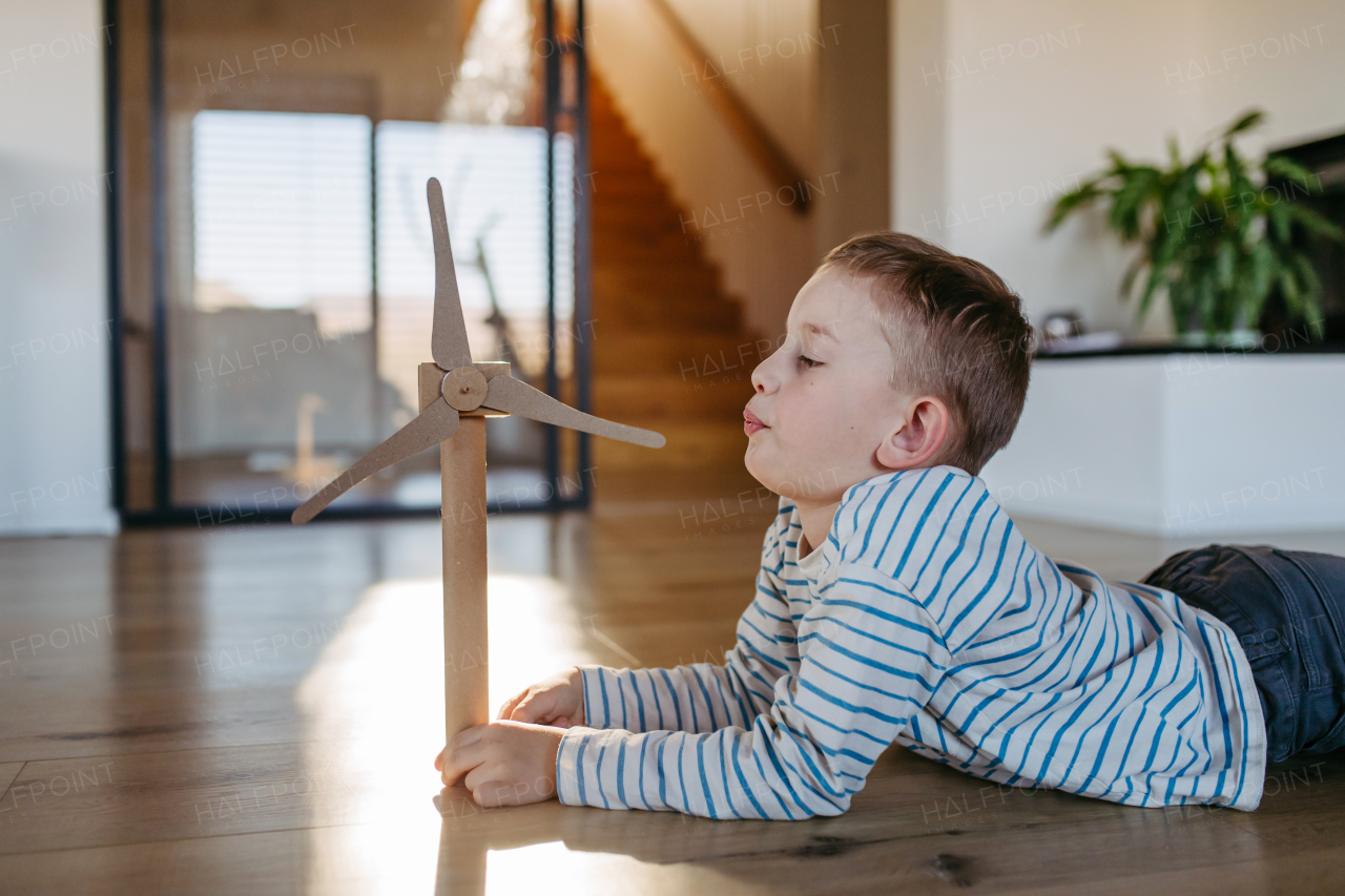 Boy blowing into blades of wind turbine model. Concpet of renewable energy sustainable lifestyle for next generations. Learning through play.