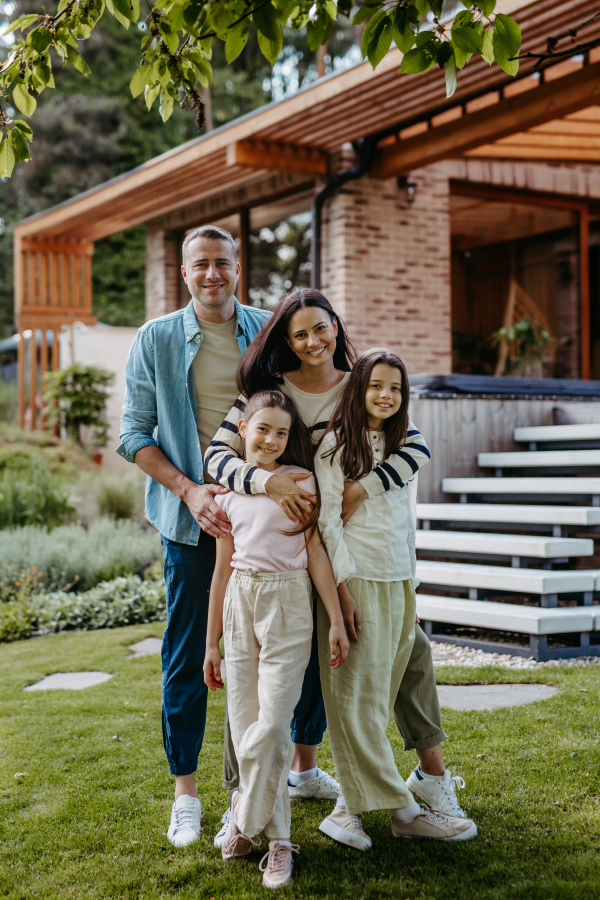 Beautfiul young family standing in front their family home enjoying together time, laughing, having fun.