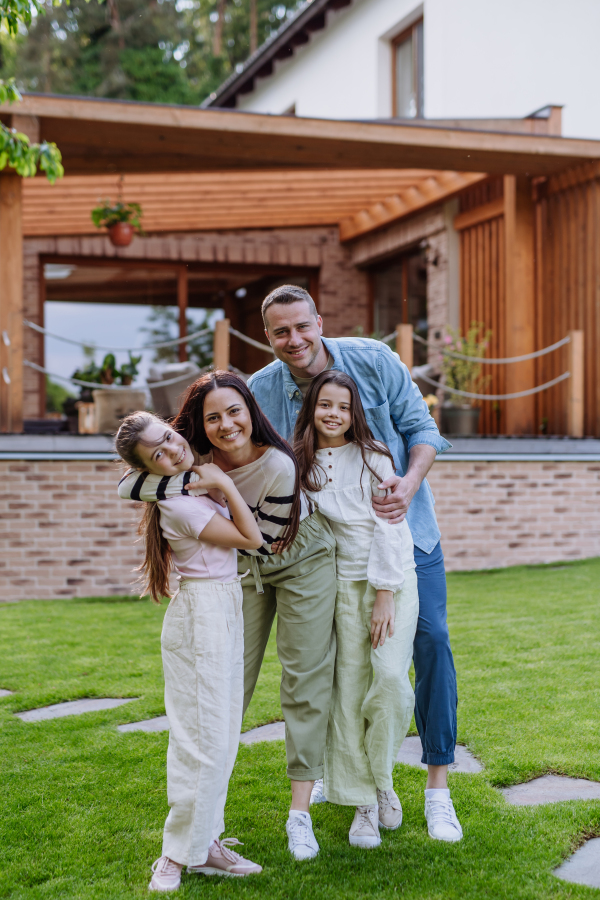 Beautfiul young family standing in front their family home enjoying together time, laughing, having fun.