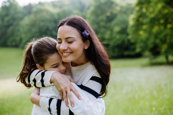 Beautiful mother with daughter, embracing or hugging, sitting in the grass at meadow. Concept of Mother's Day and maternal love.