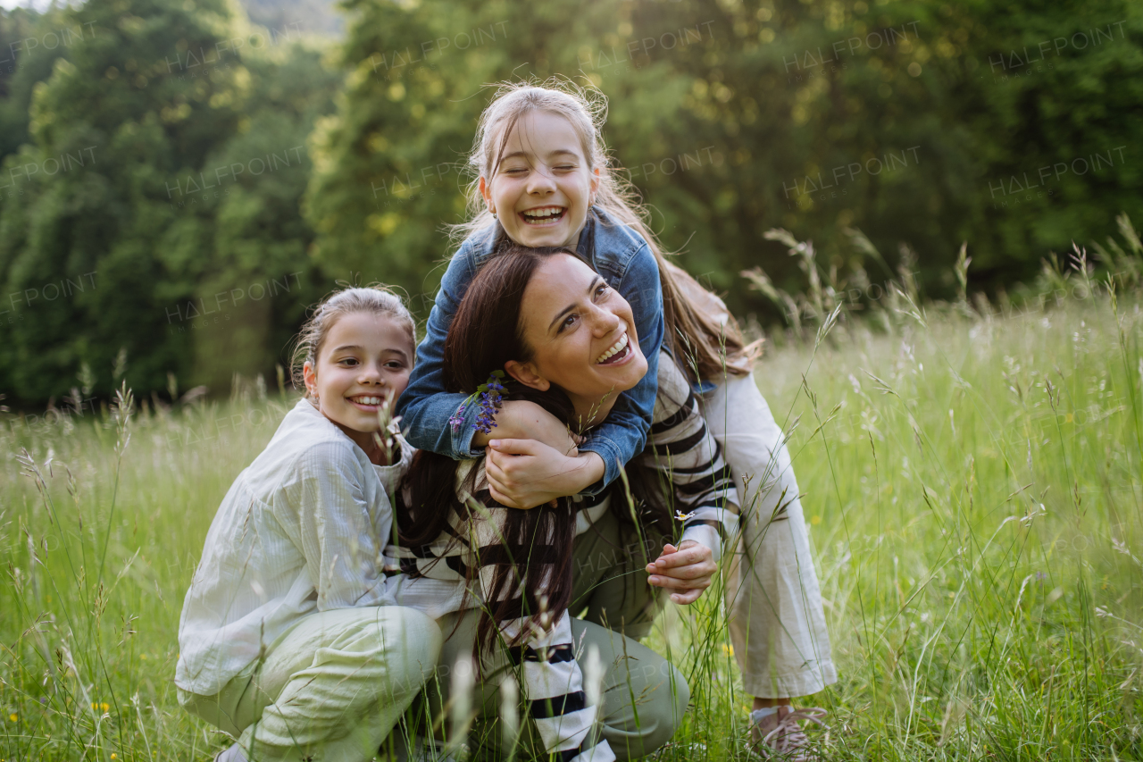 Beautiful mother with two daughters, embracing, laughing at meadow. Concept of Mother's Day and maternal love.