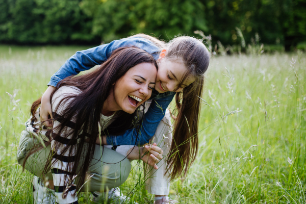 Beautiful mother with daughter, playing at the meadow, piggybacking, having fun. Concept of Mother's Day and maternal love.