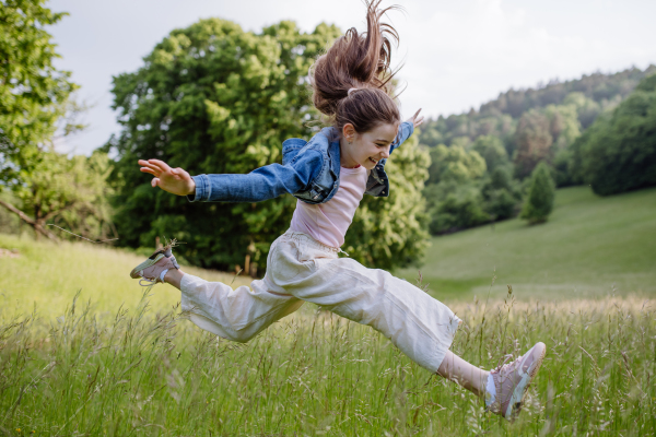 Portrait of beautiful young girl jumping in tall grass, having fun, enjoying warm spring day.