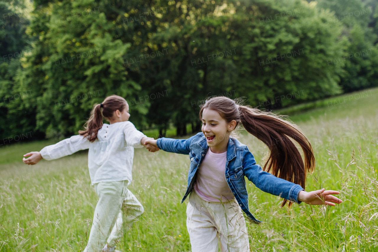 Two sisters playing at meadow in tall grass, having fun, running a laughing. Sisterly love and siblings relationship concept.