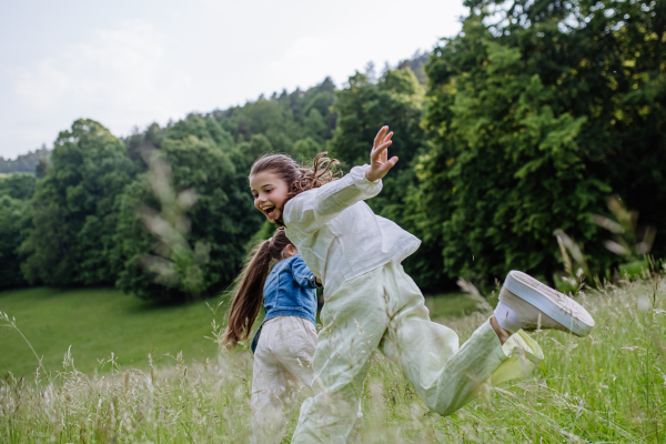 Two sisters playing at meadow in tall grass, having fun, running a laughing. Sisterly love and siblings relationship concept.