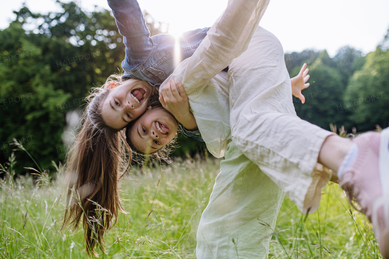 Two sisters playing at meadow in tall grass, having fun, piggybacking each other. Sisterly love and siblings relationship concept.