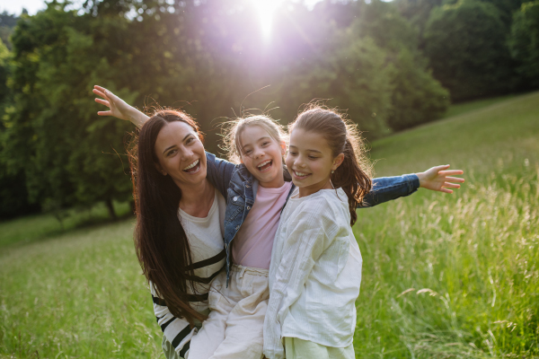 Beautiful mother with two daughters, playing at meadow, laughing, having fun. Concept of Mother's Day and maternal love.