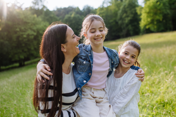 Beautiful mother with daughters, picking flowers, playing, havig fun at meadow. Concept of Mother's Day and maternal love.