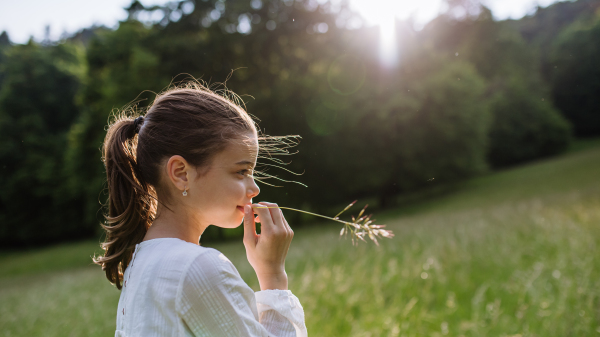 Portrait of beautiful young girl with blade of grass in her mouth, standing on meadow, enjoying warm spring day.