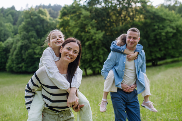 Portrait of beautiful family, parents piggibacking two daughters, having fun in the nature.