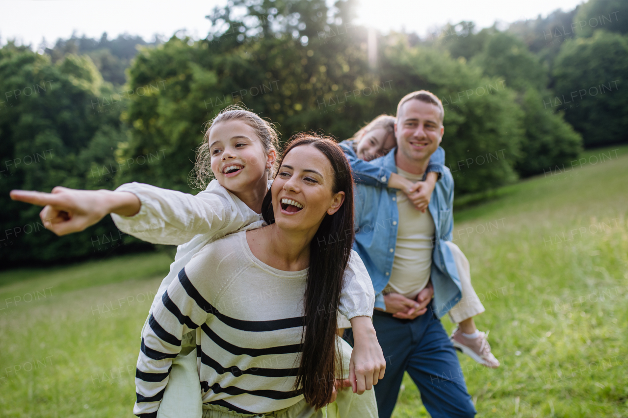 Portrait of beautiful family, parents piggibacking two daughters, having fun in the nature.