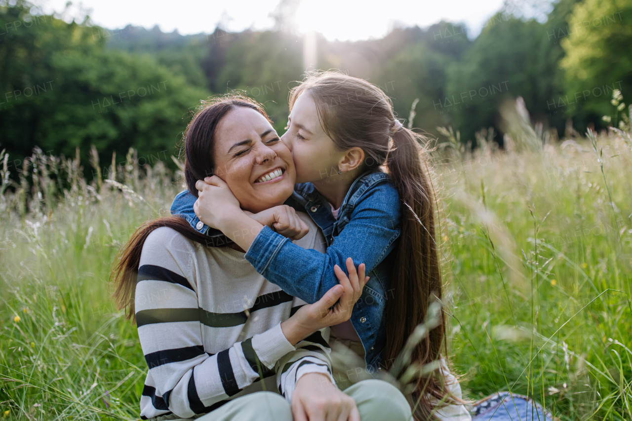 Beautiful mother with daughter, embracing or hugging, sitting in the grass at meadow. Concept of Mother's Day and maternal love.