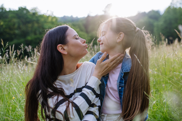 Beautiful mother with daughter, looking at each other while sitting in the grass at meadow. Concept of Mother's Day and maternal love.