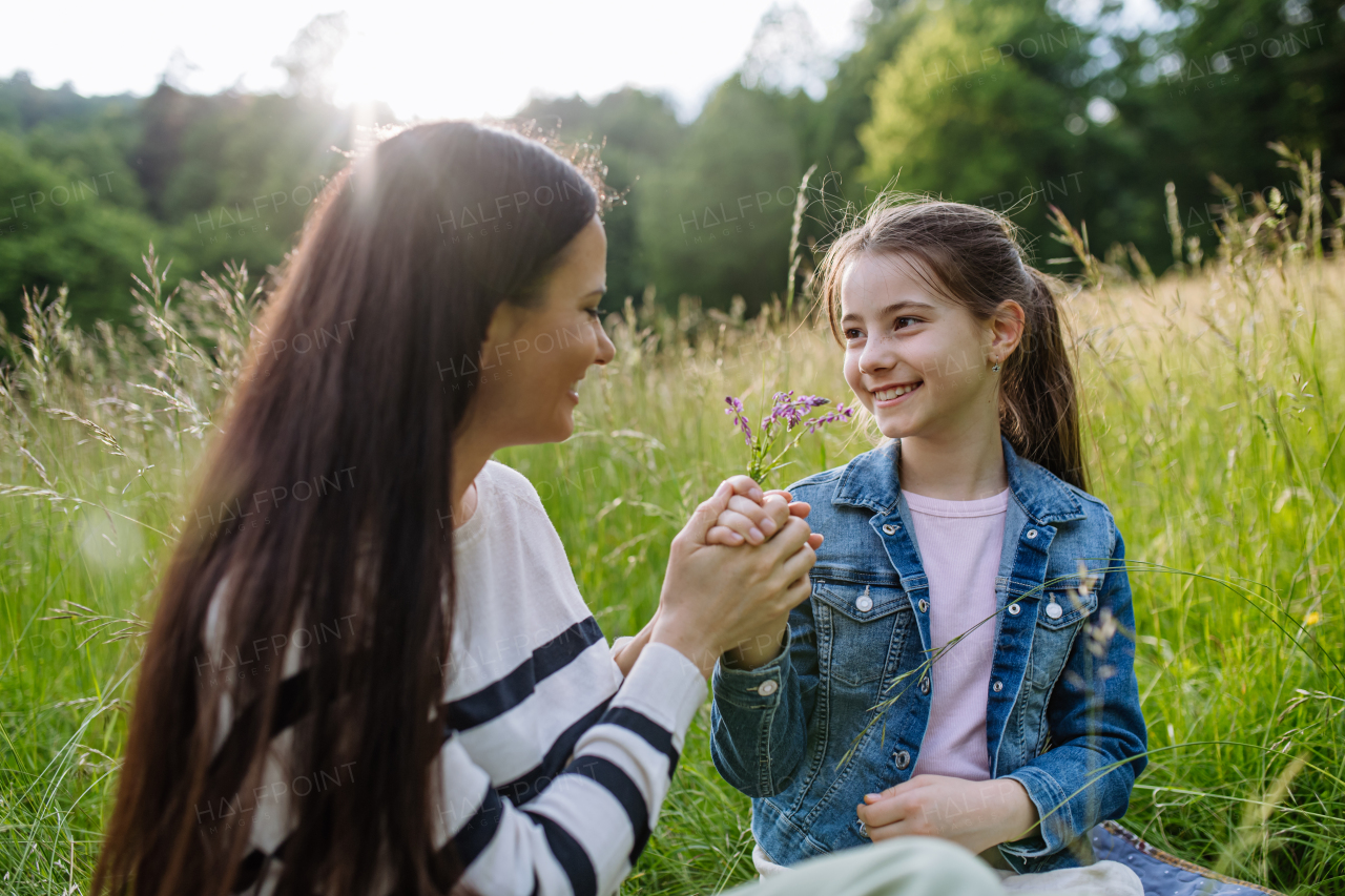 Beautiful mother with daughter, holding by hands and sitting in the grass at meadow. Concept of Mother's Day and maternal love.