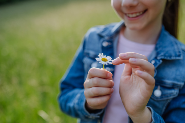 Portrait of beautiful young girl holding daisy flower, standing on meadow, enjoying warm spring day. Banner with copy space.