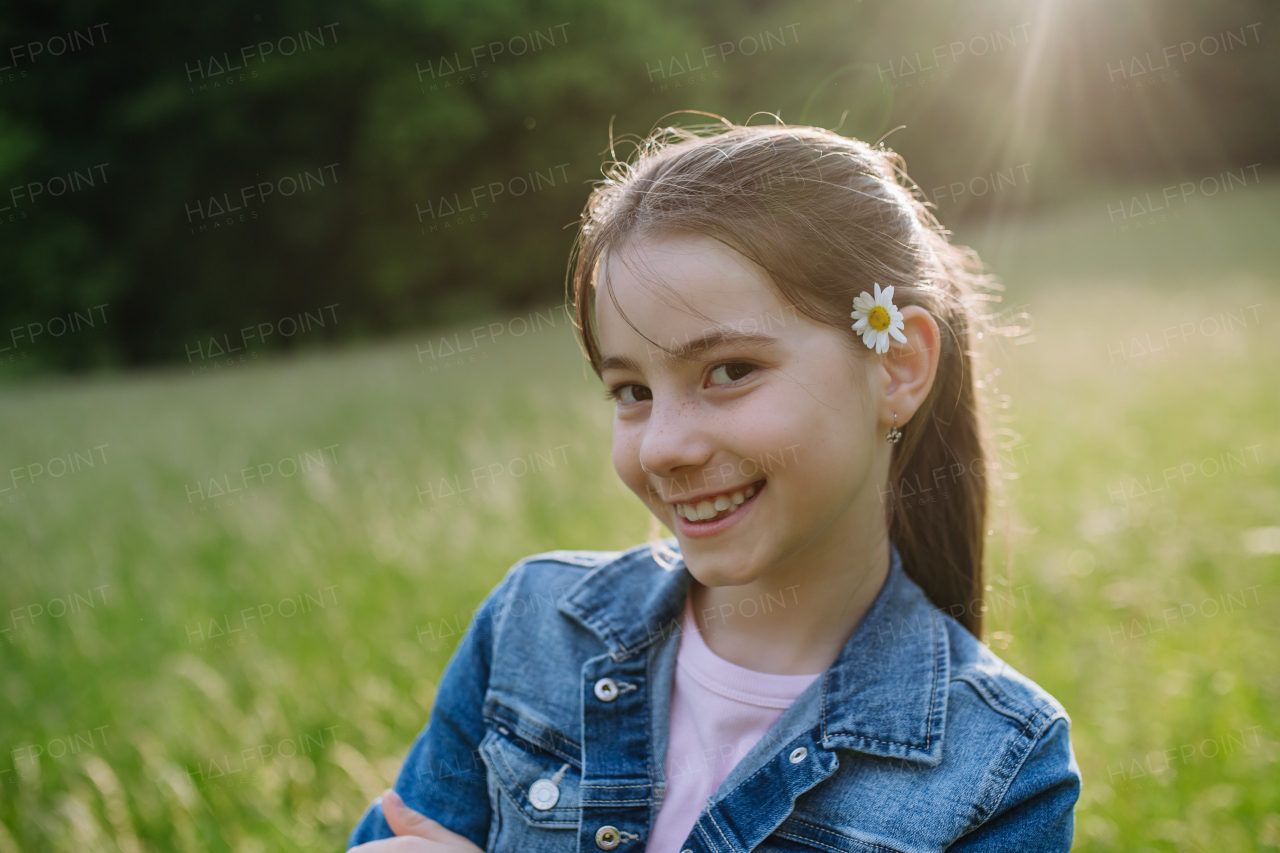 Portrait of beautiful young girl with flower behind the ear, standing on meadow, enjoying warm spring day.