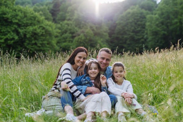 Beautfiul young family sitting in grass at meadow, enjoying together time, laughing, having fun.