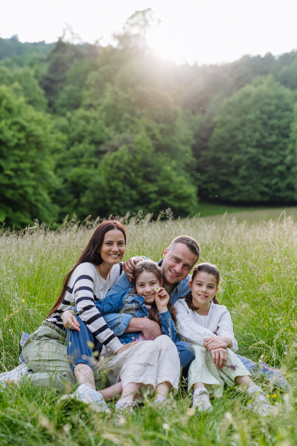 Beautfiul young family sitting in grass at meadow, enjoying together time, laughing, having fun.