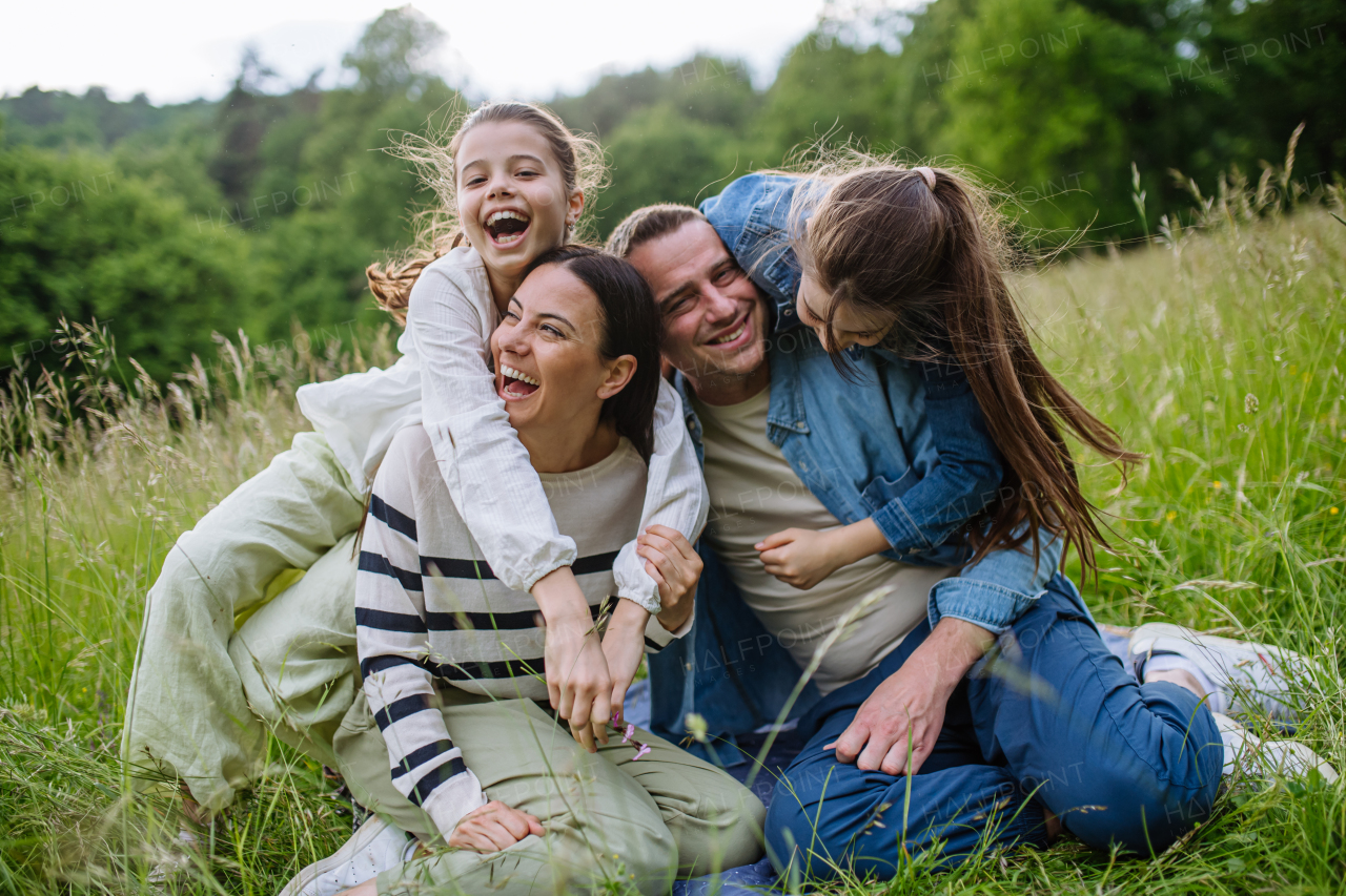 Beautfiul young family sitting in grass at meadow, enjoying together time, laughing, having fun.