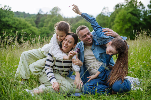 Beautfiul young family sitting in grass at meadow, enjoying together time, laughing, having fun.