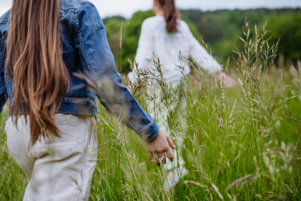 Two sisters playing at meadow in tall grass, having fun, running a laughing. Sisterly love and siblings relationship concept.