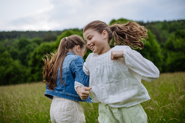 Two sisters playing at meadow in tall grass, running and dancing, having fun. Sisterly love and siblings relationship concept.