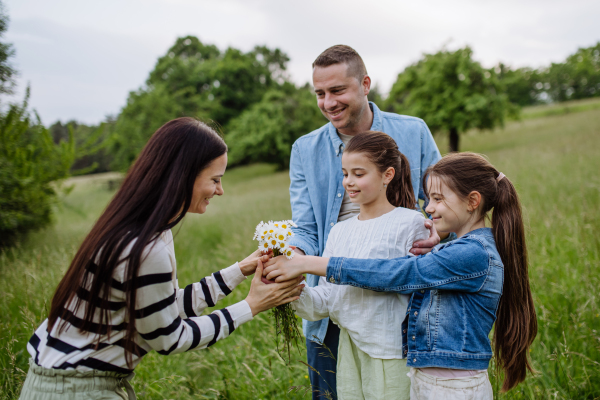 Family on walk in forest, going through meadow. Daughters picking flowers, giving them to mother. Concept of family ecological hobby in nature and Mother's Day.