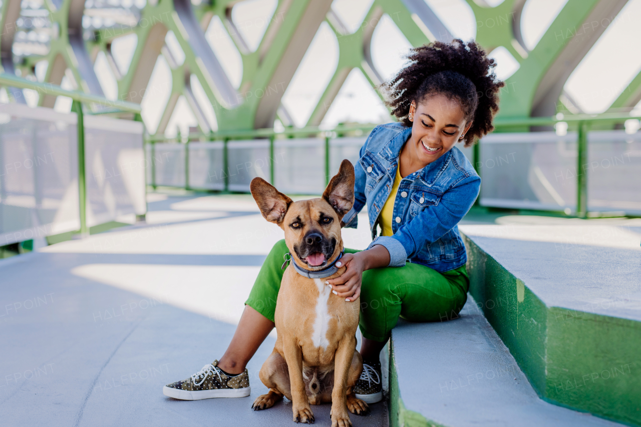 Multiracial girl sitting and resting with her dog outside in the bridge, training him, spending leisure time together. Concept of relationship between a dog and teenager, everyday life with pet.