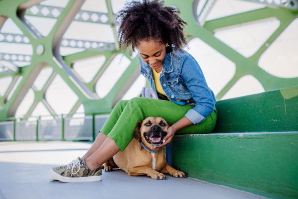 Multiracial girl sitting and resting with her dog outside in the bridge, training him, spending leisure time together. Concept of relationship between a dog and teenager, everyday life with pet.