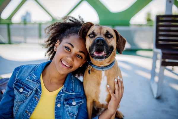 Portrait of happy multiracial girl with her dog, sitting outdoor. Concept of relationship between dog and teenager, everyday life with pet.