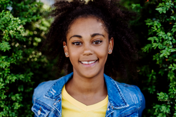 Portrait of young happy multiracial teenage girl with afro hair, standing outdoor in park.