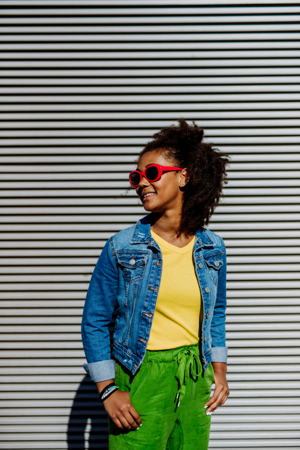 Young happy multiracial teenage girl with red sunglasses and afro hairstyle, standing outdoor.