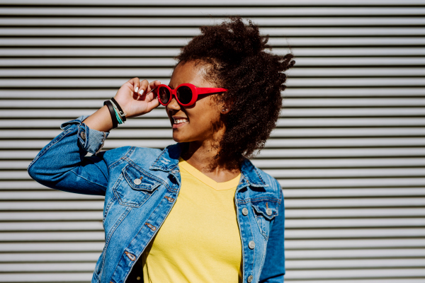 Portrait of young happy multiracial teenage girl with red sunglasses and afro hairstyle, standing outdoor.