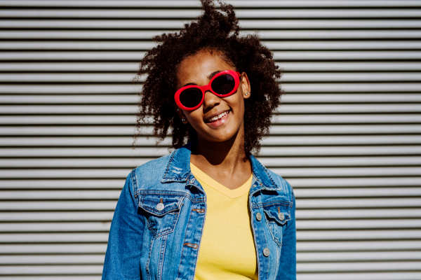 Portrait of young happy multiracial teenage girl with red sunglasses and afro hairstyle, standing outdoor.