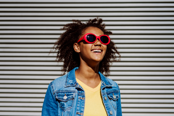 Portrait of young happy multiracial teenage girl with red sunglasses and afro hairstyle, standing outdoor.